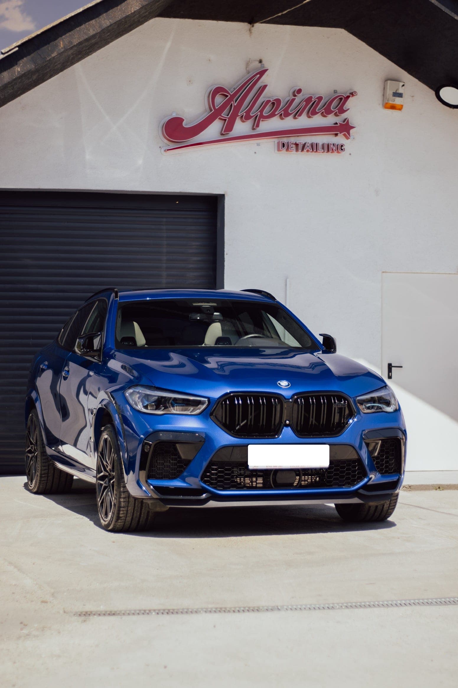 BMW X5 M albastru parcat în fața atelierului Alpina Detailing, cu sigla pe fațadă